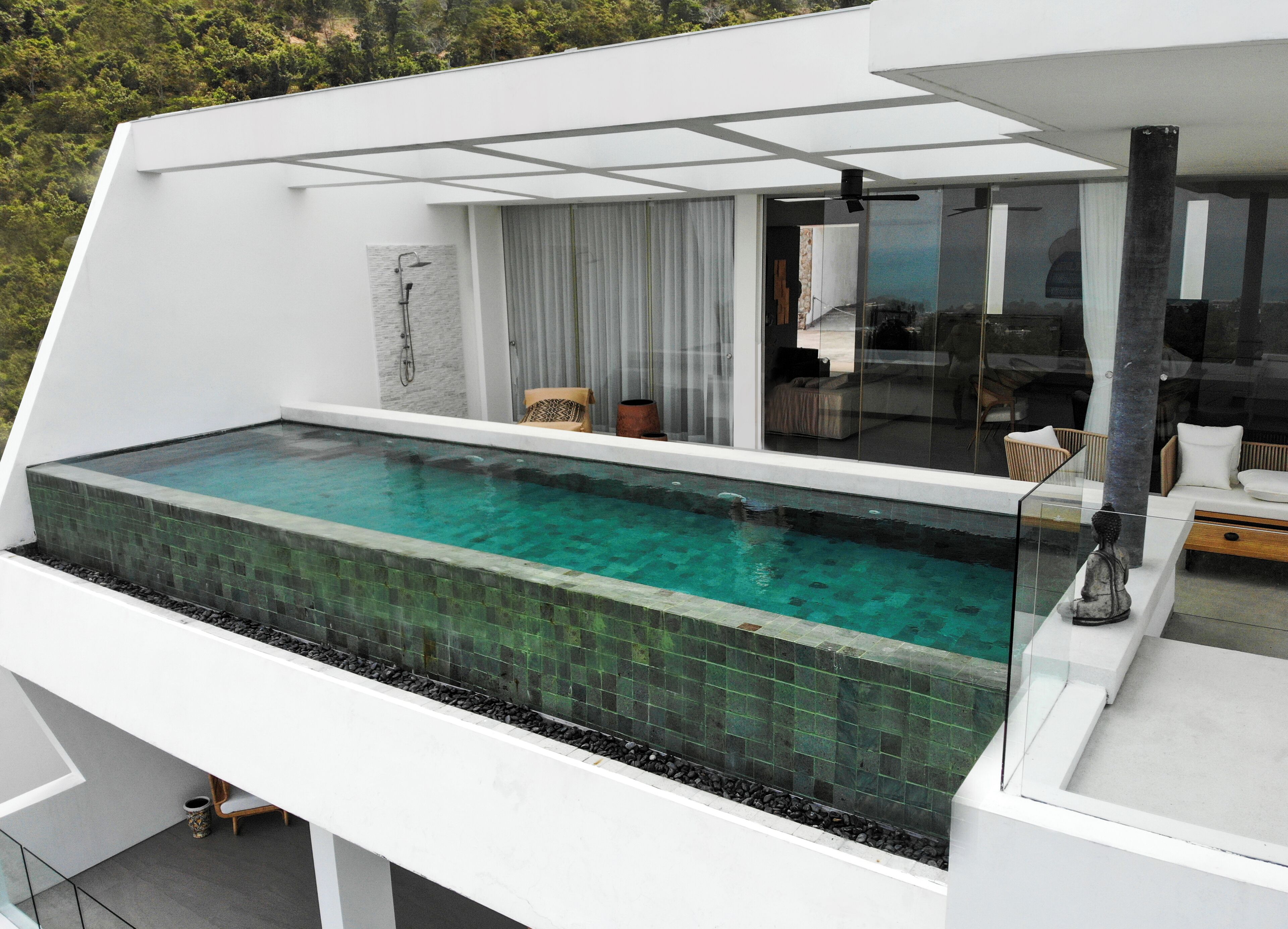 Une piscine à débordement moderne offrant une vue dégagée sur le ciel, dotée d’une balustrade en verre et d’un espace de détente extérieur au design minimaliste.