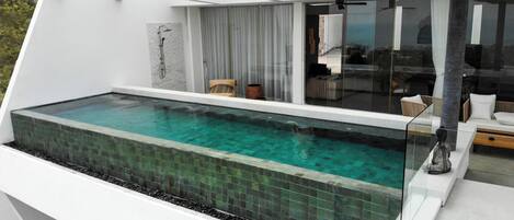 Une piscine à débordement moderne offrant une vue dégagée sur le ciel, dotée d’une balustrade en verre et d’un espace de détente extérieur au design minimaliste.