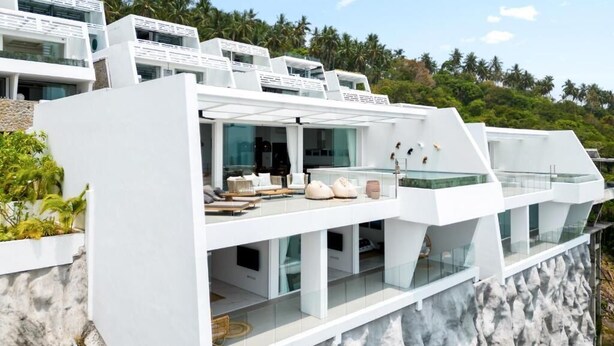 A modern multi-story building with balconies, large windows, and a view of palm trees. - Golden Lotus Villas (Koh Samui)