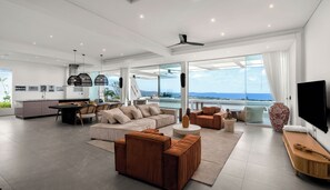 A modern living space with a kitchen, dining area, and seating with a view of the ocean. - Golden Lotus Villas (Koh Samui)