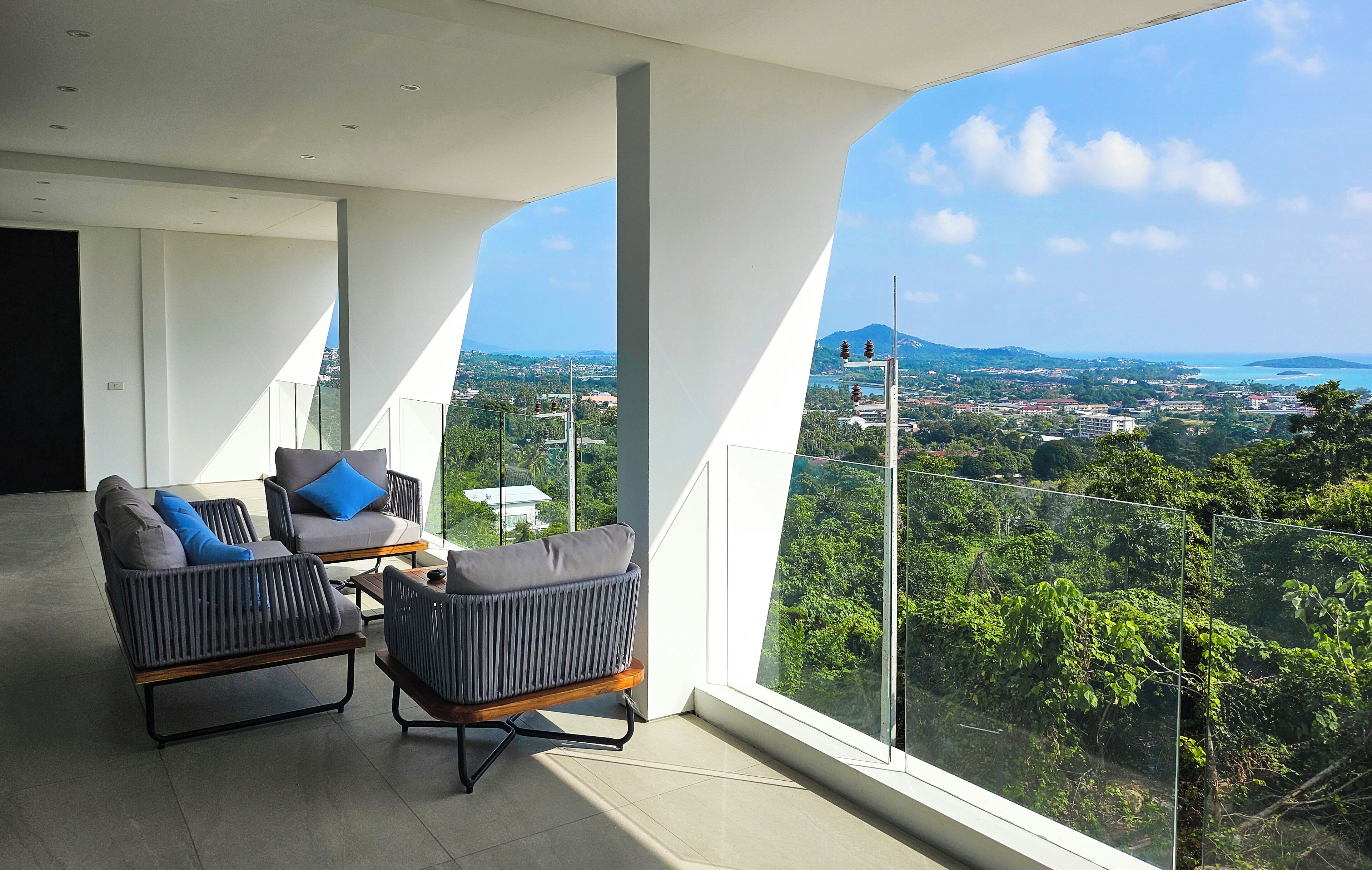 En moderne balkon med to grå sofaer og et bord, der giver udsigt over by og grønne områder.