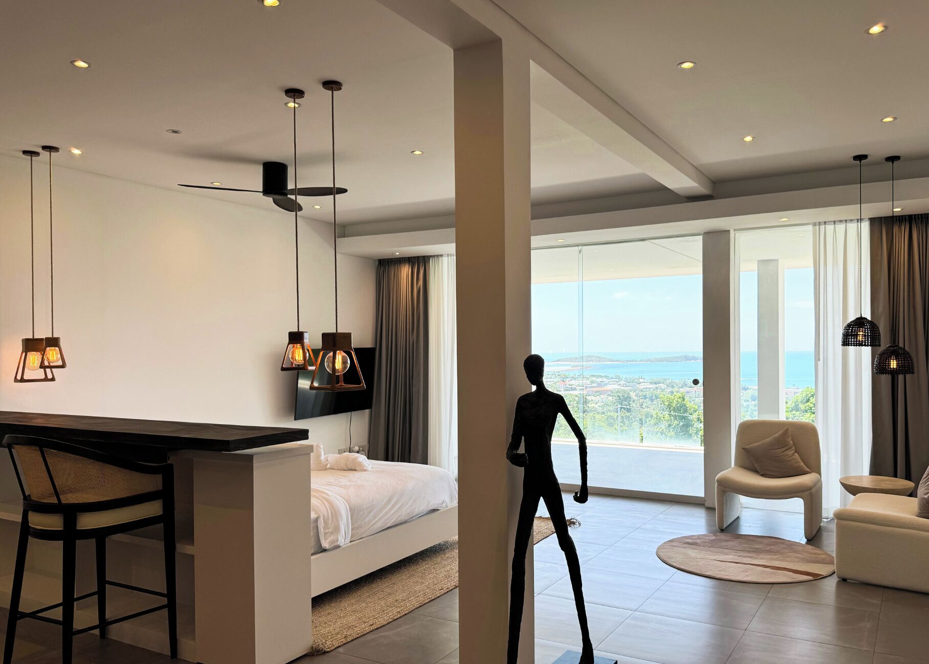 Een moderne hotelkamer met een bed, een bureau, een stoel, een bank en uitzicht op zee.