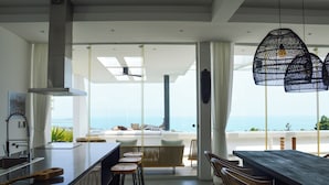 A modern kitchen with a large island, bar stools, and a view of the ocean. - Golden Lotus Villas (Koh Samui)