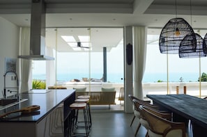 A modern kitchen with a large island, bar stools, and a view of the ocean. - Golden Lotus Villas (Koh Samui)