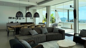 A modern living room with a large sofa, a dining area, and a balcony with a view. - Golden Lotus Villas (Koh Samui)