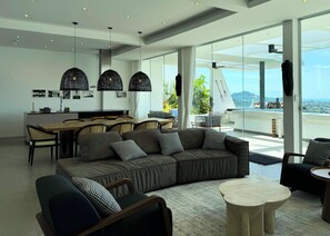 A modern living room with a large sofa, a dining area, and a balcony with a view. - Golden Lotus Villas (Koh Samui)