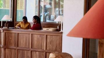 A reception desk with two staff members, a wooden panel design, and a lamp.