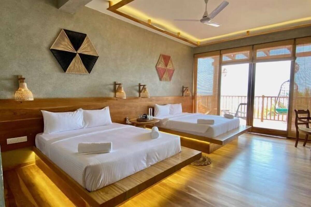 A hotel room with two beds, a ceiling fan, and a large sliding glass door leading to a balcony.