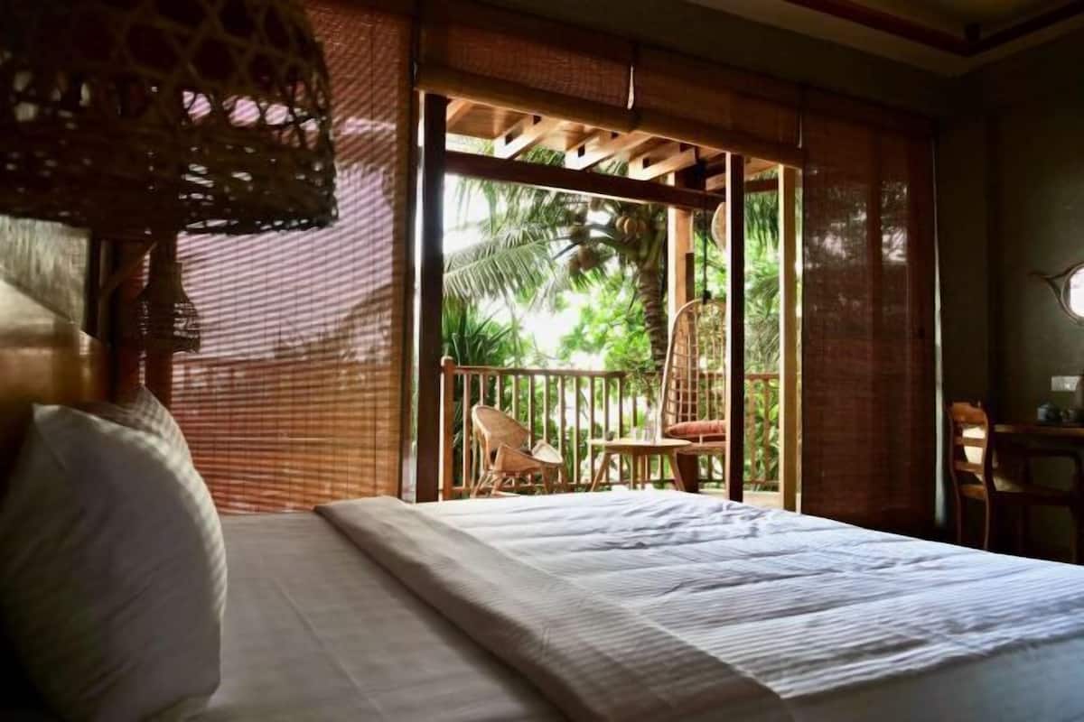 A bedroom with a bed, a chair, a table, and a view of greenery outside.