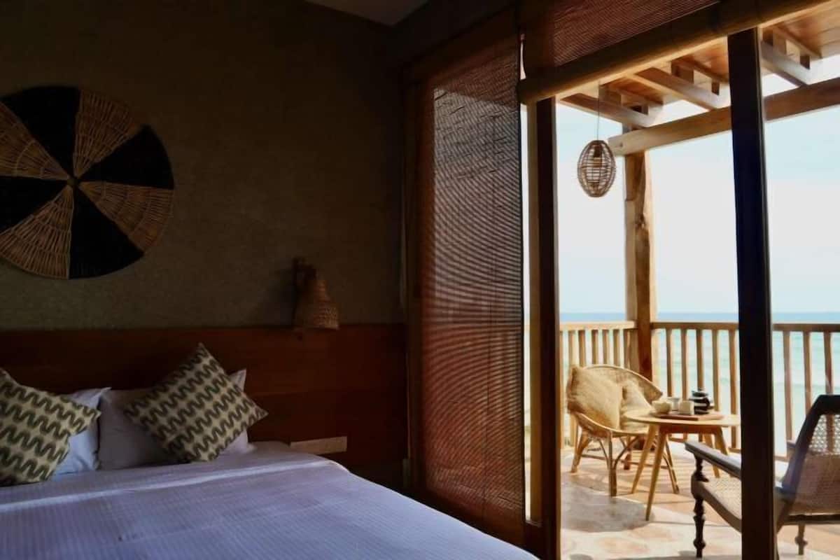 A bedroom with a bed, pillows, a wall art piece, and a view of an outdoor balcony with a chair and table.