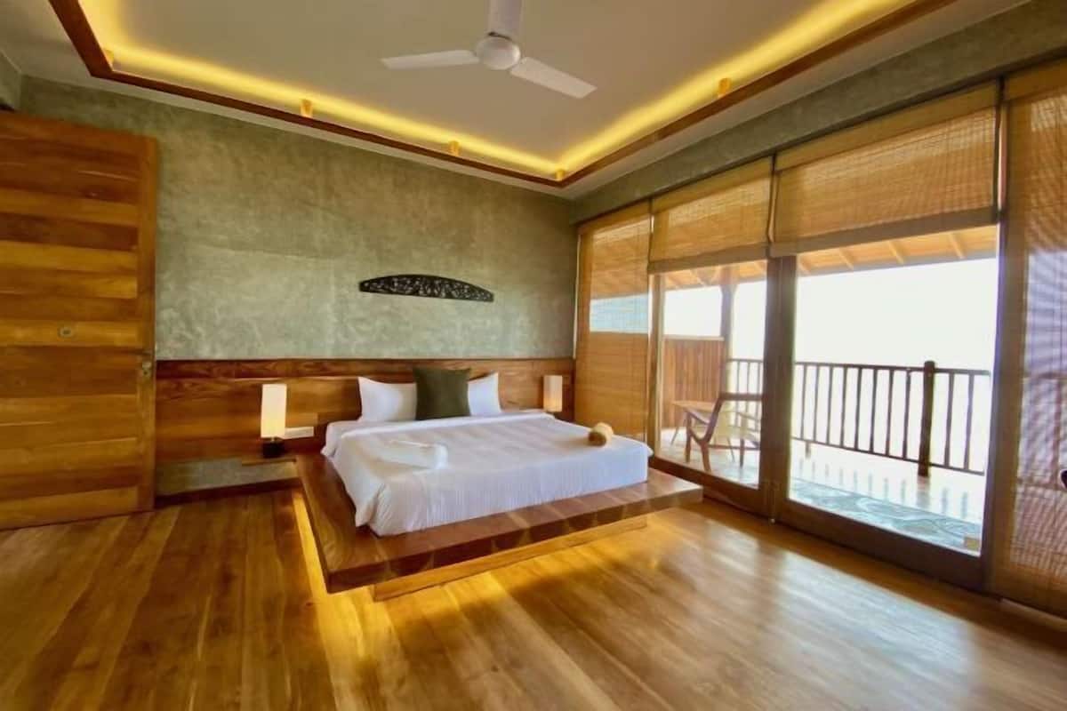 A bedroom with a bed, wooden walls, a ceiling fan, and large windows.