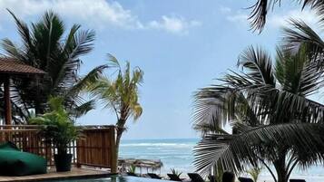 A pool area with a view of the ocean, surrounded by palm trees and a wooden structure.