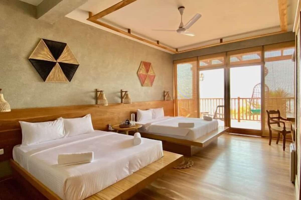 A hotel room with two beds, a ceiling fan, a large window, and a balcony.