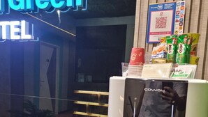 Un espace d'accueil d'hôtel équipé d'un distributeur d'eau, d'un panneau lumineux néon indiquant « HÔTEL ÉCOLO », et d'un code QR donnant accès aux services.