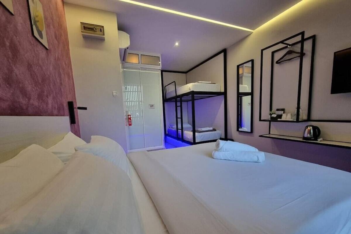 A hotel room with a bunk bed, a single bed, a wardrobe, a mirror, and a shelf with toiletries.