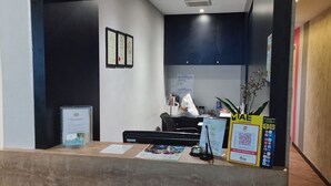 Un espace d’accueil comprenant un comptoir, des chaises, des certificats encadrés et un panneau indiquant un service national de codes QR.