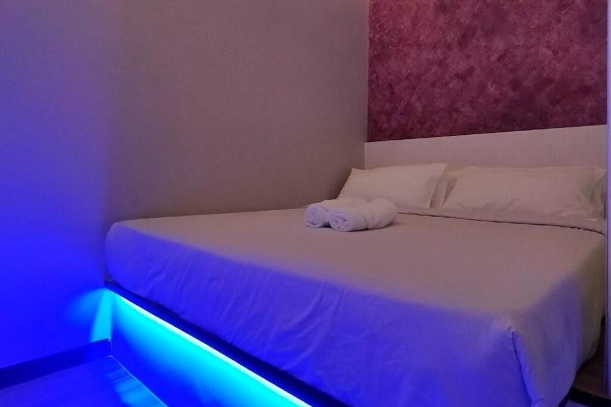 A neatly made bed with white linens and two rolled towels, a marble-patterned headboard, and a blue ambient light strip along the bed's edge.