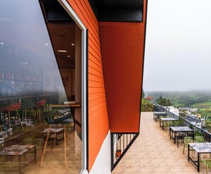 Un balcon agrémenté de tables et de chaises, donnant sur une vallée parsemée de maisons.