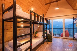 Un intérieur en bois avec des lits superposés, un balcon offrant une vue et un sac à dos posé sur le sol.