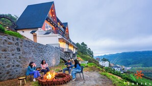 A building with a stone wall, a fire pit, and a view of the surrounding landscape. - Zostel Kodaikanal (Vilpatti) (Kodaikanal)