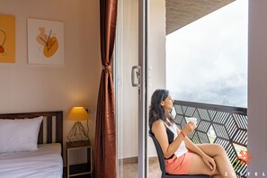 Une chambre avec un lit, une table de chevet avec une lampe, une fenêtre avec des rideaux et un balcon avec vue.