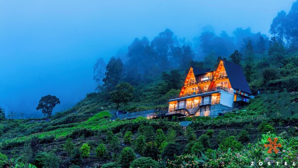 A two-story building with a steep roof, surrounded by lush greenery and misty mountains. - Zostel Kodaikanal (Vilpatti) (Kodaikanal)