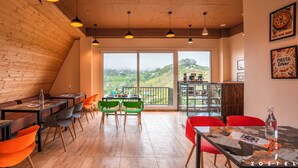 A restaurant with wooden walls, large windows, and a view of the countryside. - Zostel Kodaikanal (Vilpatti) (Kodaikanal)