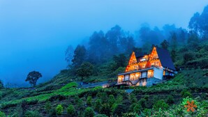 Un bâtiment à deux étages, doté d’un toit en pente, entouré d’une végétation luxuriante et de montagnes brumeuses.