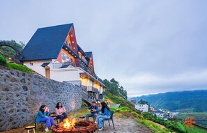 A building with a stone wall, a fire pit, and a view of the surrounding landscape. - Zostel Kodaikanal (Vilpatti) (Kodaikanal)