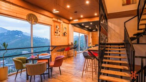 Un intérieur moderne avec un escalier en bois, un coin repas avec des chaises et une vue sur l’extérieur.