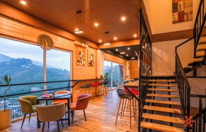 A modern interior with a wooden staircase, a dining area with chairs, and a view of the outdoors. - Zostel Kodaikanal (Vilpatti) (Kodaikanal)