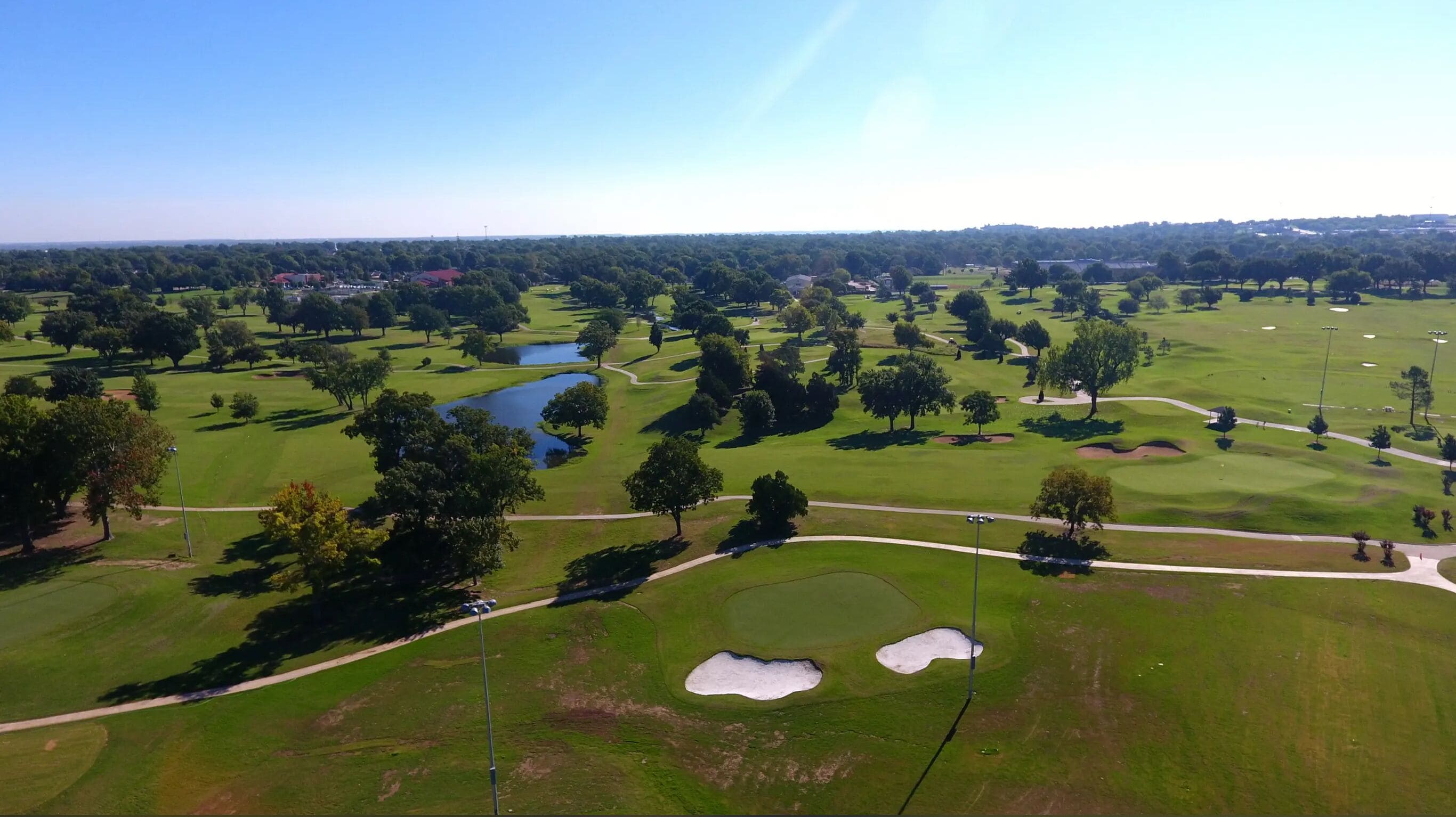 An aerial view of a golf course with multiple holes, water bodies, and trees.