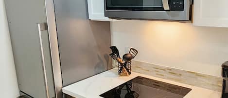 A modern kitchen with a stainless steel refrigerator, a built-in microwave, and an induction cooktop.