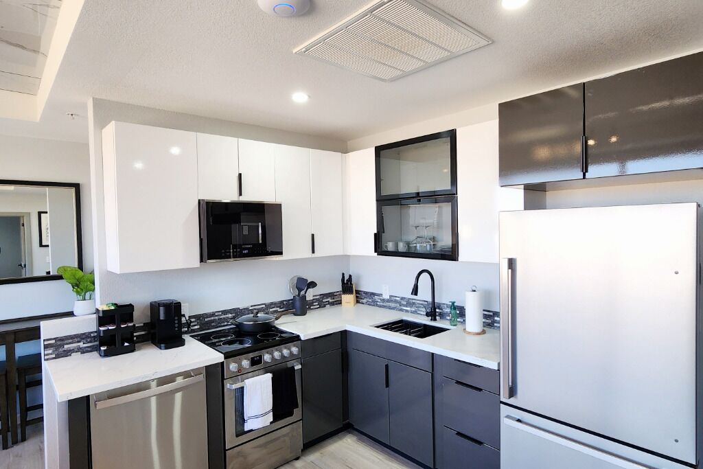 A modern kitchen with white and black cabinetry, stainless steel appliances, and a tiled backsplash.