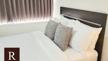A neatly made bed with a dark headboard, white bedding, and two gray pillows.