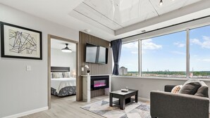 A modern living room with a fireplace, a flat-screen TV, a sofa, and a large window offering a city view. - Reese Tower (Tulsa)