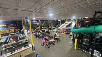 An indoor amusement park with various attractions, including a green slide and multiple tables and chairs for visitors.