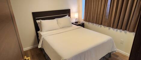 Un dormitorio con una cama grande, una mesita de noche, un ventilador de techo y una ventana con cortinas.