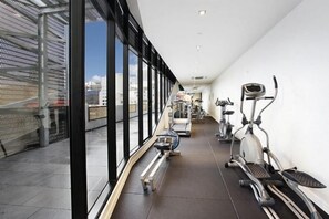 A gym with exercise equipment and large windows overlooking a cityscape. - Chic Apartment by Southern Cross, FREE Parking (Melbourne)