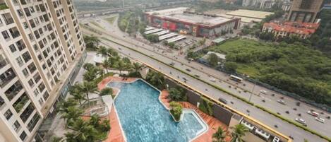 A high-rise building with a rooftop pool, surrounded by greenery and a busy road.