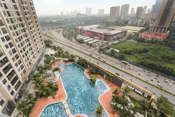 A high-rise building with a rooftop pool, surrounded by greenery and a busy road. - Vinhomes D'Capitale - Luxury Kane Aparment In Ha Noi (Hanoi)