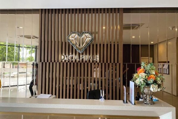 A reception desk with a wooden slat partition, a heart-shaped logo above the word "DROCAPITAL," and a vase of flowers on the counter. - Vinhomes D'Capitale - Luxury Kane Aparment In Ha Noi (Hanoi)