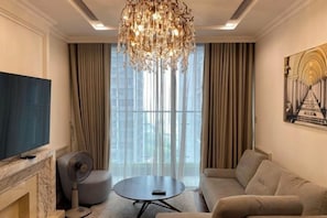 A modern living room with a fireplace, a round coffee table, a sofa, a television, and a chandelier. - Vinhomes D'Capitale - Luxury Kane Aparment In Ha Noi (Hanoi)