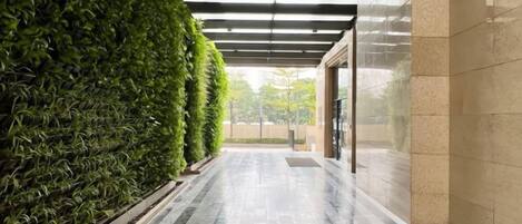 Un pasillo con un jardín vertical verde en un lateral y suelo de baldosas.