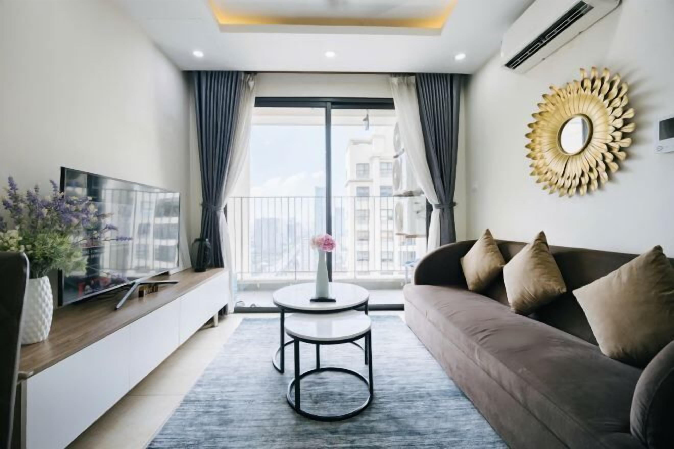 A modern living room with a sofa, a round table, a TV, and a large window with curtains.