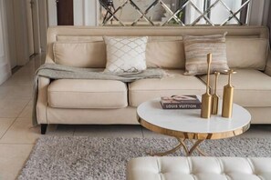 Un canapé beige agrémenté de coussins à motifs, une table basse ronde aux pieds dorés et un livre de la marque Louis Vuitton.