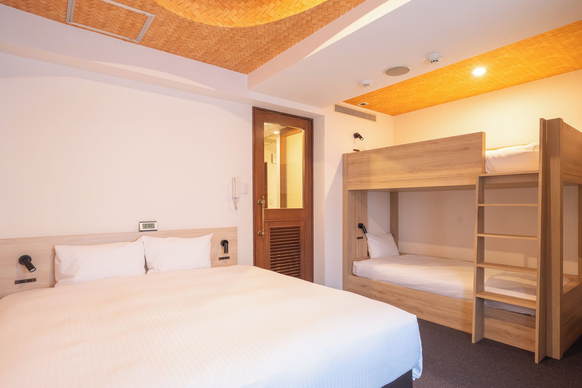 A hotel room with a large bed, a wooden bunk bed, a mirror, a phone, and a ceiling light.