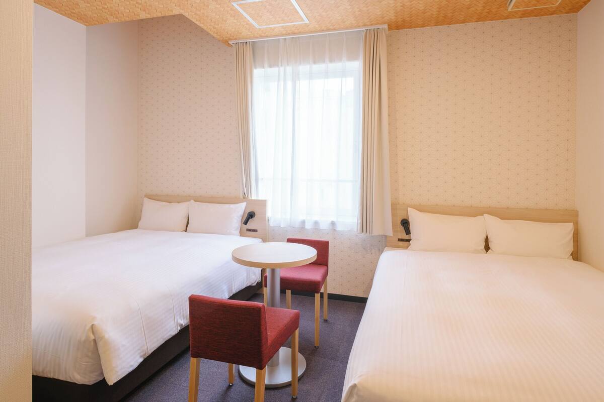 Een hotelkamer met twee bedden, een klein rond tafeltje en een rode stoel.
