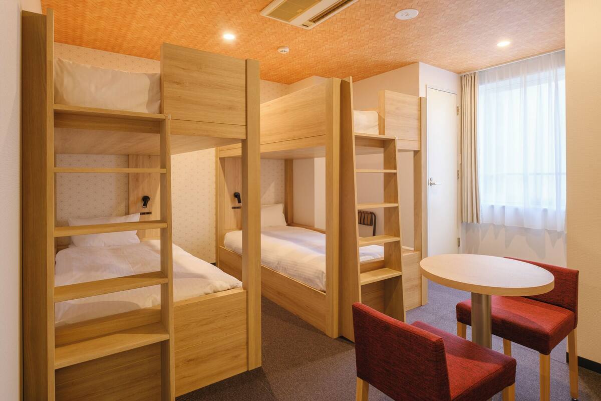 Een kamer met stapelbedden, een ronde tafel en twee rode stoelen.