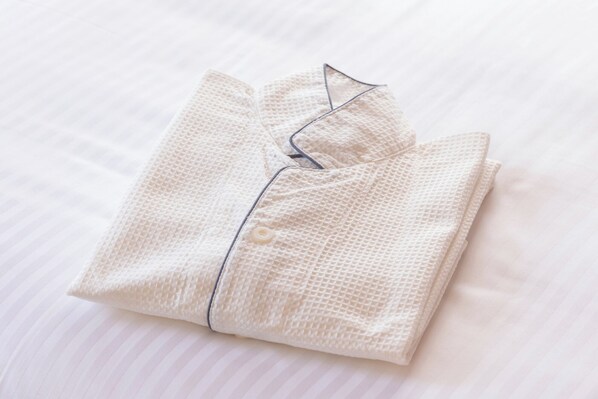 Una camisa blanca impecablemente doblada, con un botón y cuello, sobre una cama blanca con diseño a rayas.